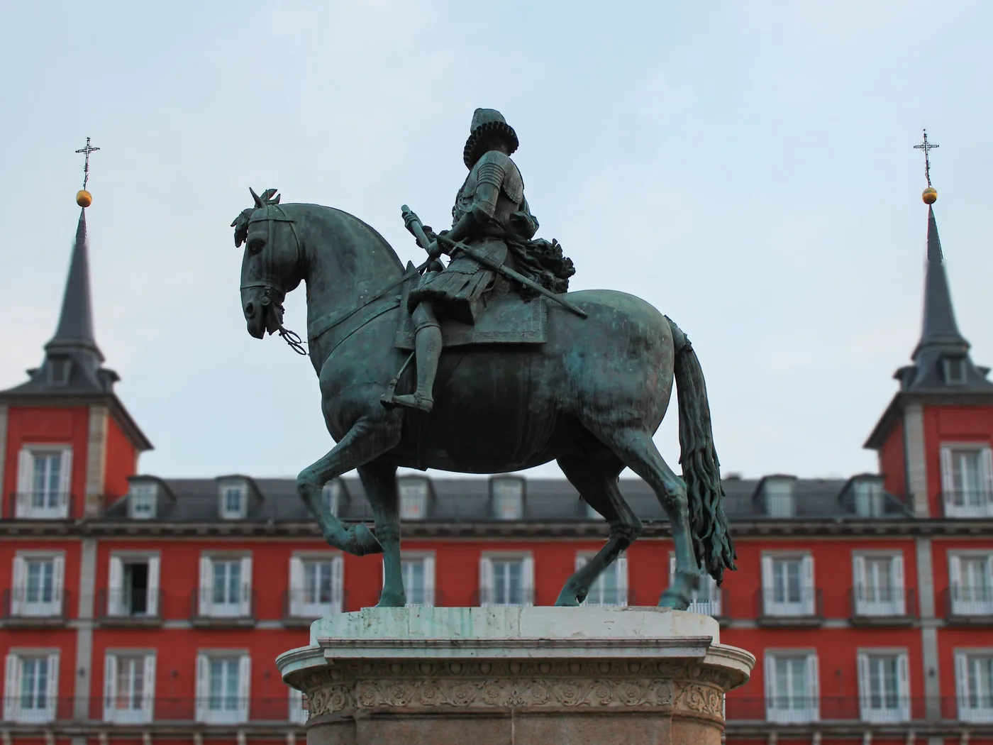 The bronze equestrian statue of Philip III against the red facade and slate spires of Plaza Mayor in Madrid.